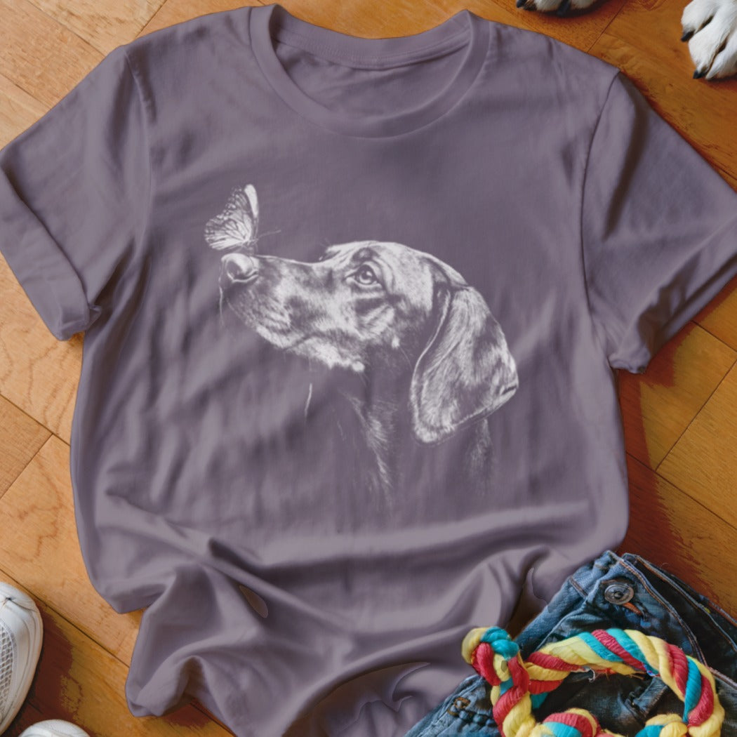 Dusty purple t-shirt featuring a white line drawing of a dog looking at a butterfly.