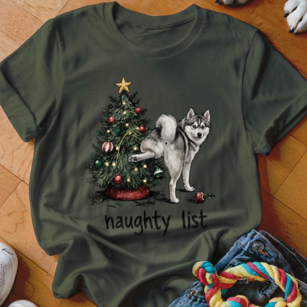 Husky next to Christmas tree with "naughty list" text on green t-shirt.
