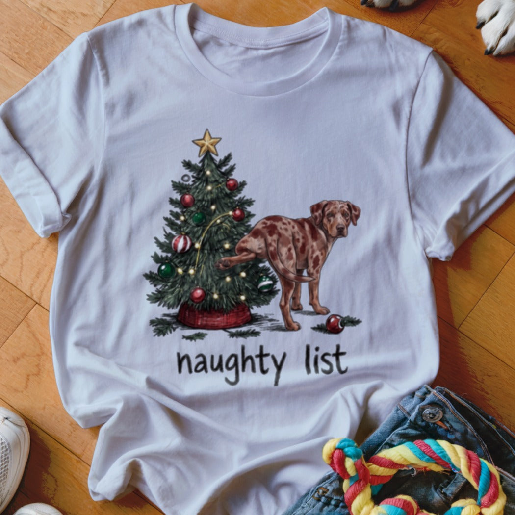 White t-shirt featuring a graphic of a dog lifting its leg on a Christmas tree with the text "naughty list".