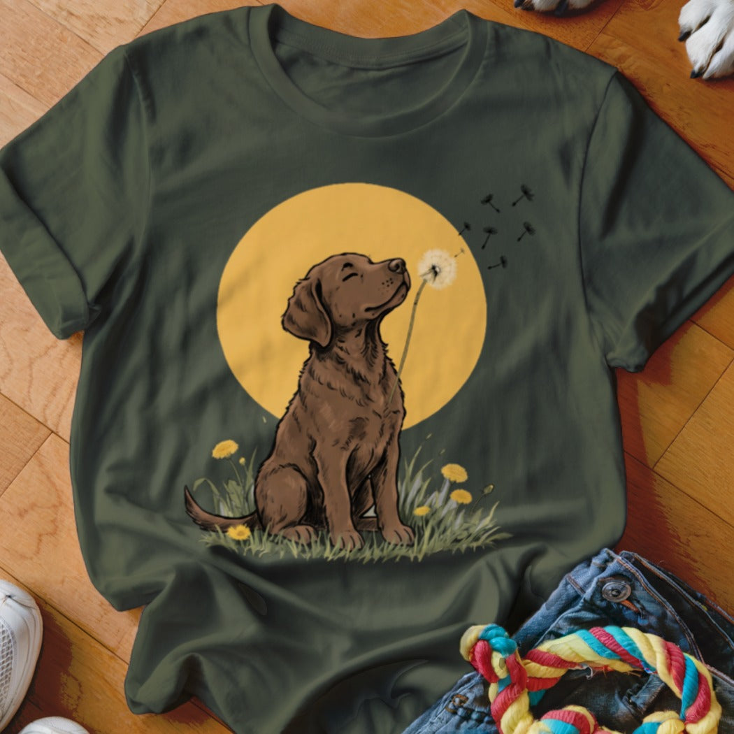Dark green t-shirt featuring an illustration of a brown dog sitting before a yellow sun and blowing dandelions.