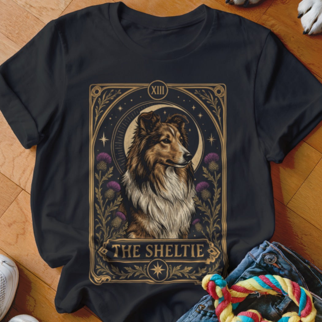 Black t-shirt featuring a tarot-style graphic of a Sheltie dog surrounded by thistles and stars, with the text "The Sheltie".