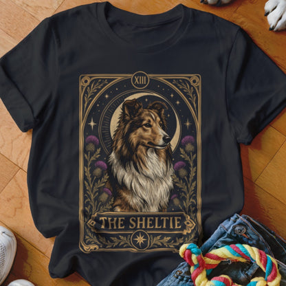 Black t-shirt featuring a tarot-style graphic of a Sheltie dog surrounded by thistles and stars, with the text "The Sheltie".