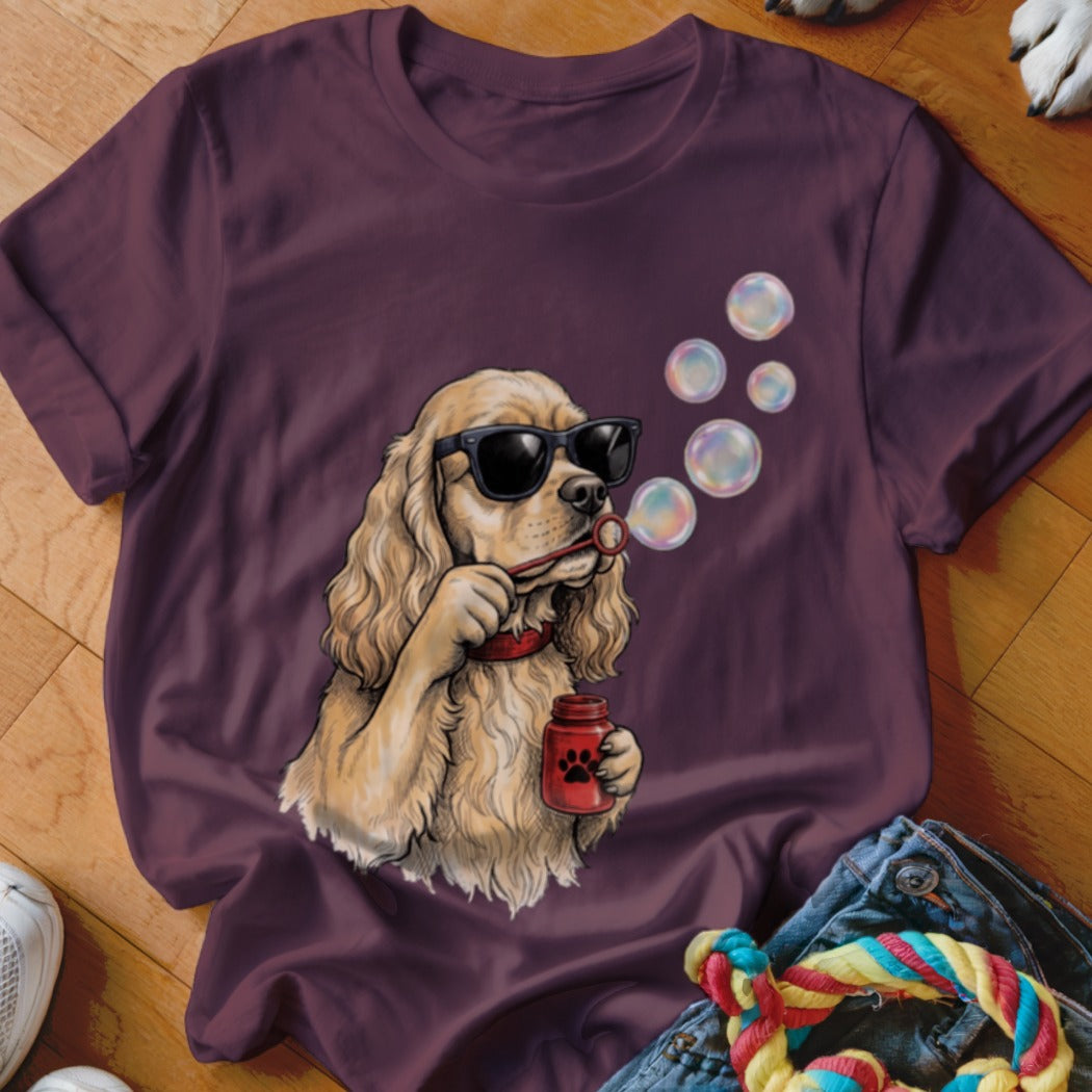 Maroon t-shirt featuring an illustration of a dog wearing sunglasses and blowing soap bubbles.