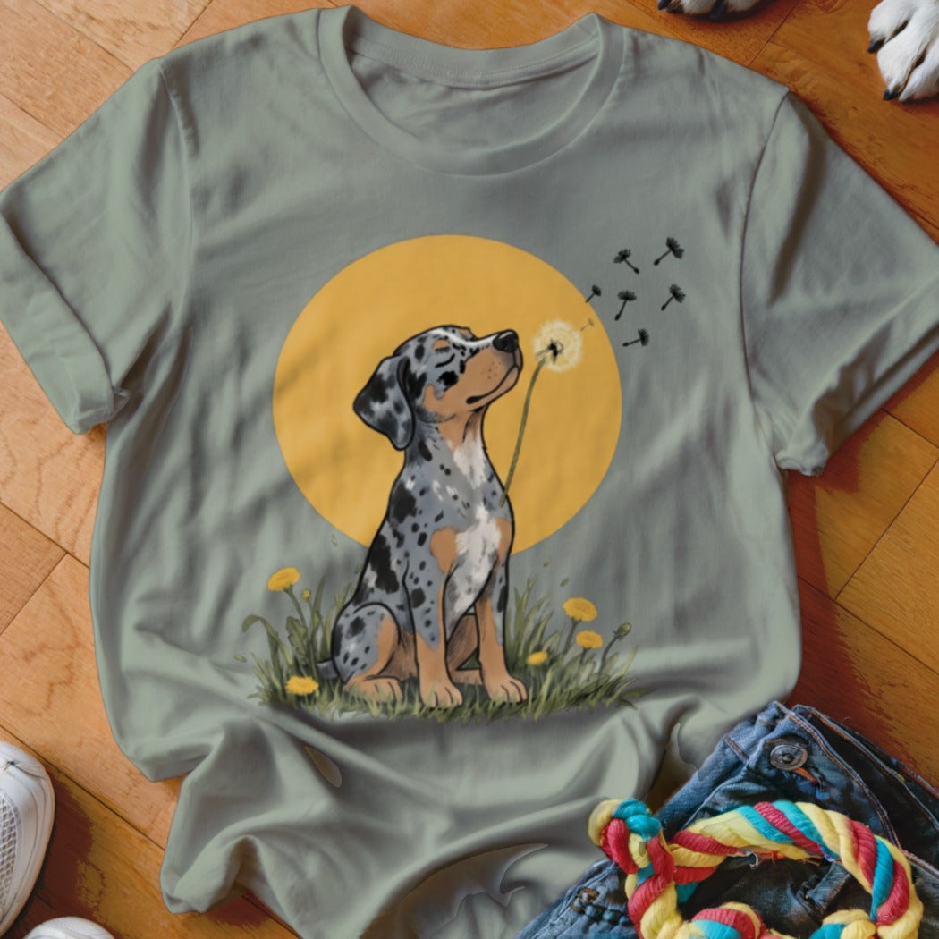 Sage green t-shirt with a graphic of a blue merle dog blowing dandelion seeds.