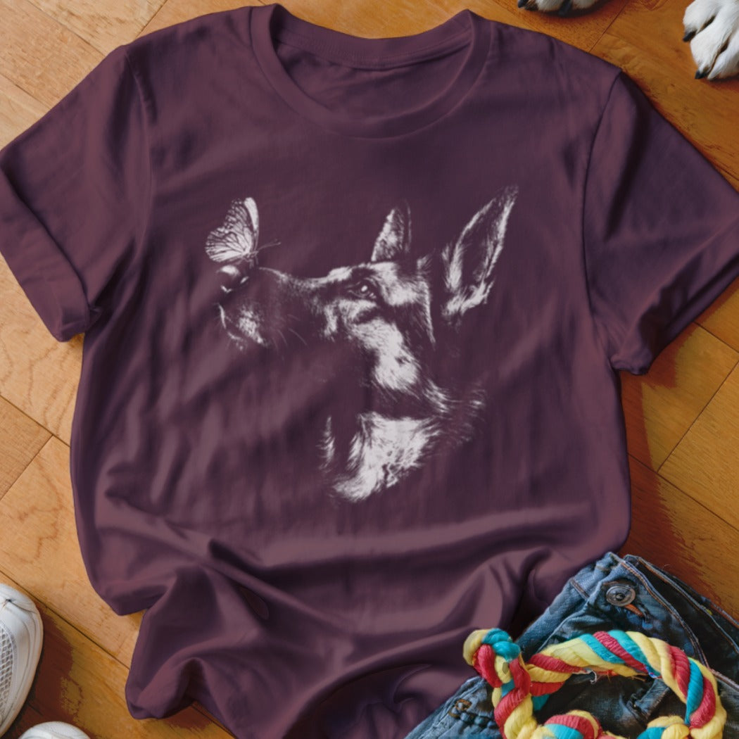 A dark purple t-shirt featuring a white sketch graphic of a German Shepherd looking at a butterfly on its nose.