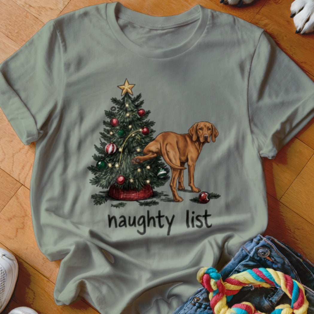 Sage green t-shirt with a graphic of a brown dog urinating on a Christmas tree, with the text naughty list.