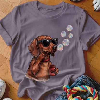 A dusty purple t-shirt features a graphic of a dachshund wearing sunglasses and blowing bubbles.
