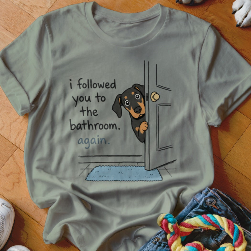 T-shirt with illustration of dog peeking through door, saying "I followed you to the bathroom. Again."
