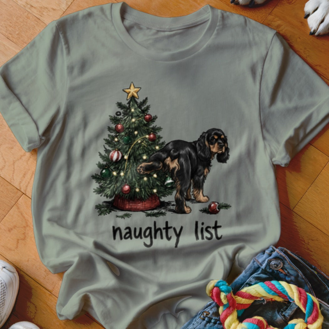 T-shirt graphic of a dog lifting leg on a Christmas tree with "naughty list" text.