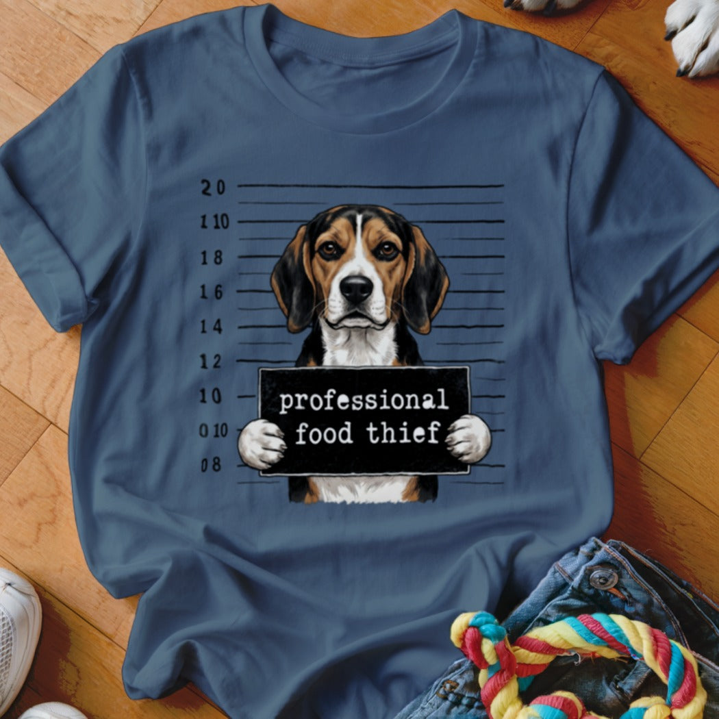 Beagle dog mugshot with "professional food thief" sign on blue t-shirt.