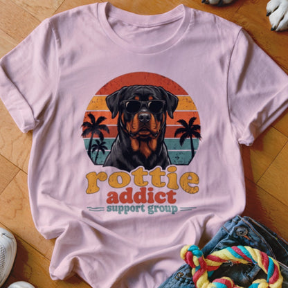 A pink t-shirt featuring a Rottweiler wearing sunglasses against a sunset graphic and palm trees.