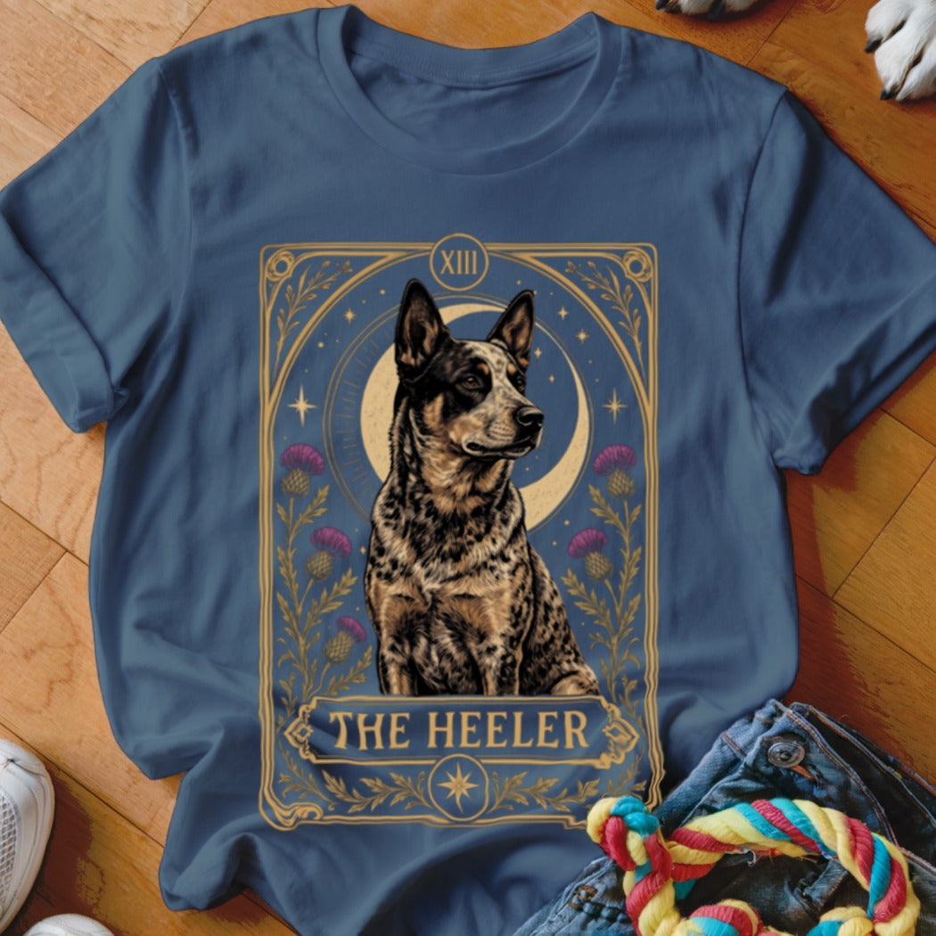 A blue t-shirt printed with a tarot card graphic featuring a cattle dog and the text The Heeler.