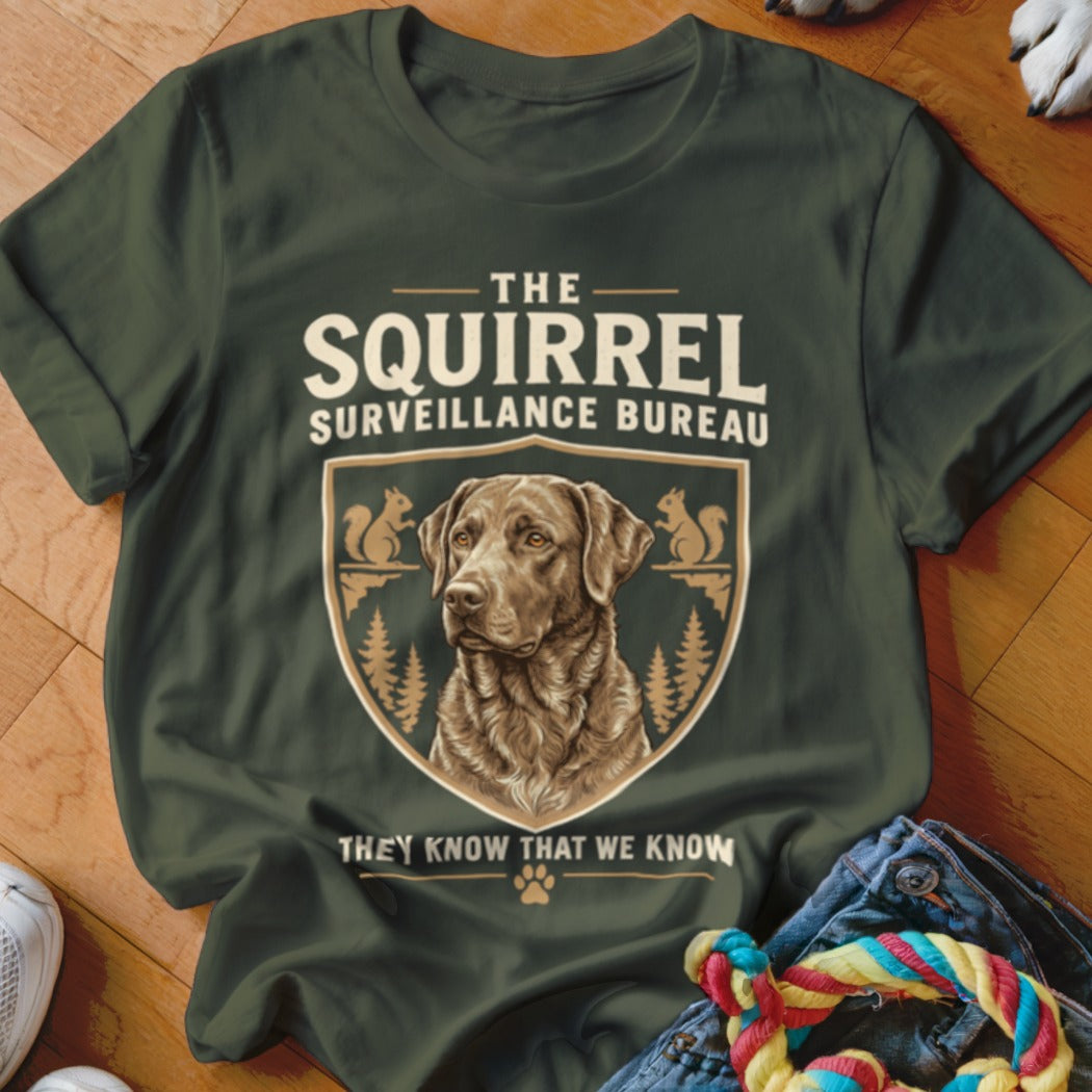 Dark green t-shirt with a vintage graphic of a brown dog inside a shield and the text The Squirrel Surveillance Bureau.