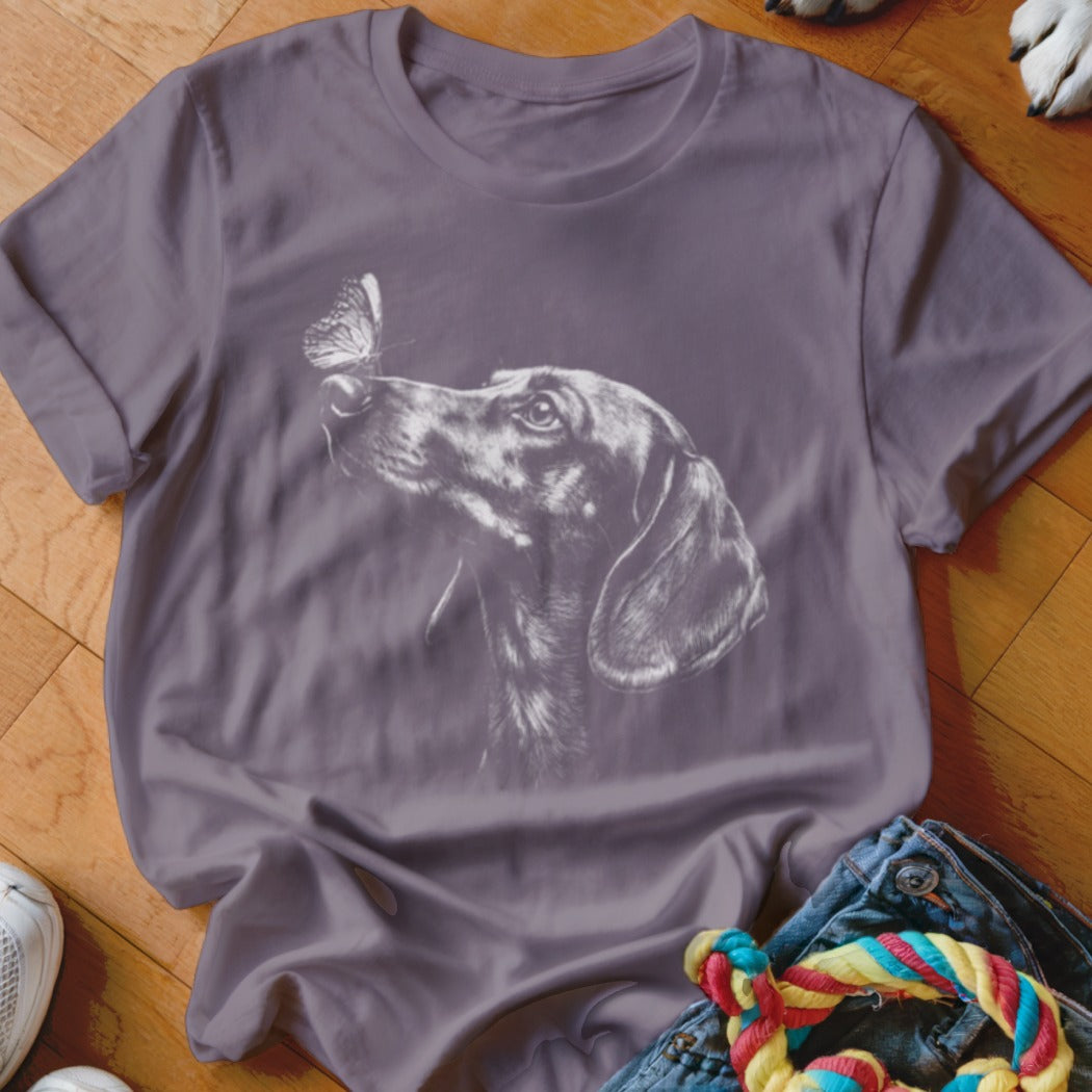 Purple short-sleeve t-shirt featuring a white sketch of a dachshund dog looking at a butterfly on its nose.