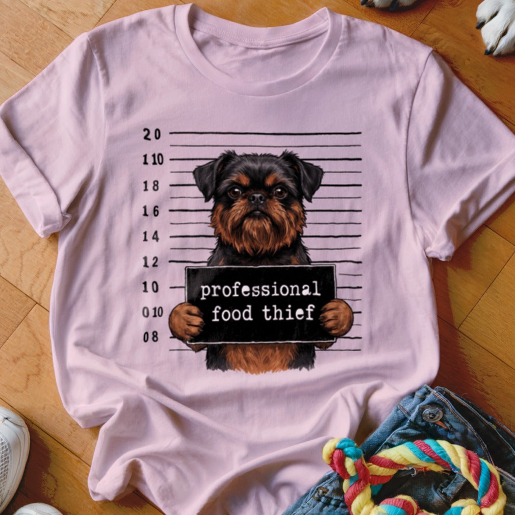 Griffon dog mugshot with "professional food thief" sign on a pink t-shirt.