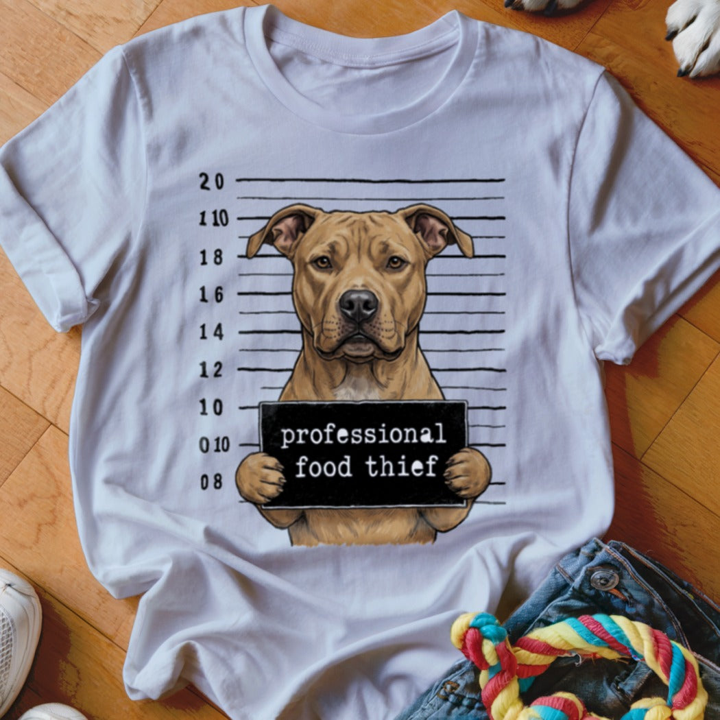 Pit bull dog mugshot with "professional food thief" sign on t-shirt.