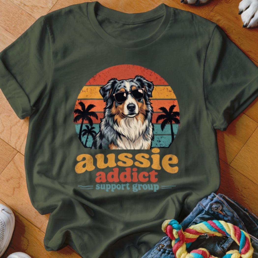 Dark green t-shirt featuring a retro graphic of an Australian Shepherd wearing sunglasses before palm trees and a sunset.