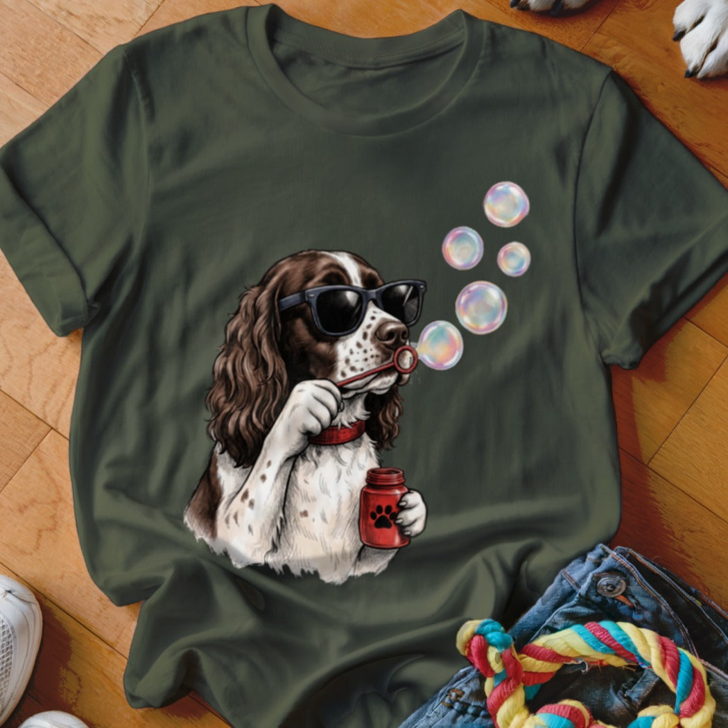 An olive green t-shirt featuring a graphic of a dog in sunglasses blowing soap bubbles.