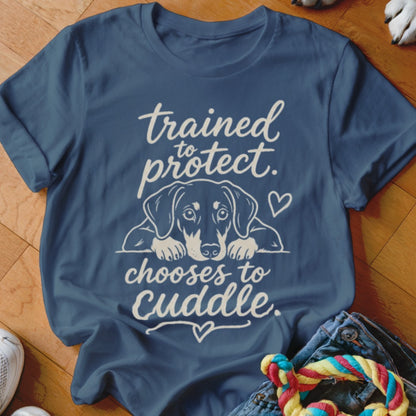 Blue t-shirt with a graphic of a dog and text "trained to protect. chooses to cuddle."