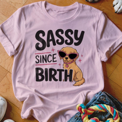 Light pink t-shirt with a graphic of a dog wearing sunglasses and text that says "SASSY SINCE BIRTH".