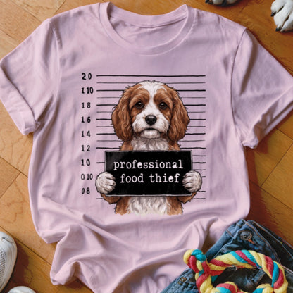 Dog mugshot with "professional food thief" sign on a pink t-shirt.