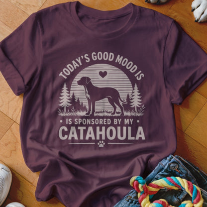 A maroon t-shirt with a graphic of a dog, trees, sun, and text reading Today’s Good Mood Is Sponsored By My Catahoula.