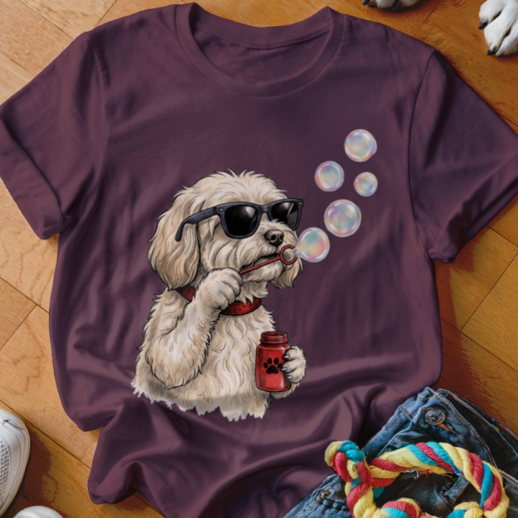 A dark purple t-shirt featuring a graphic of a fluffy white dog wearing sunglasses and blowing soap bubbles.