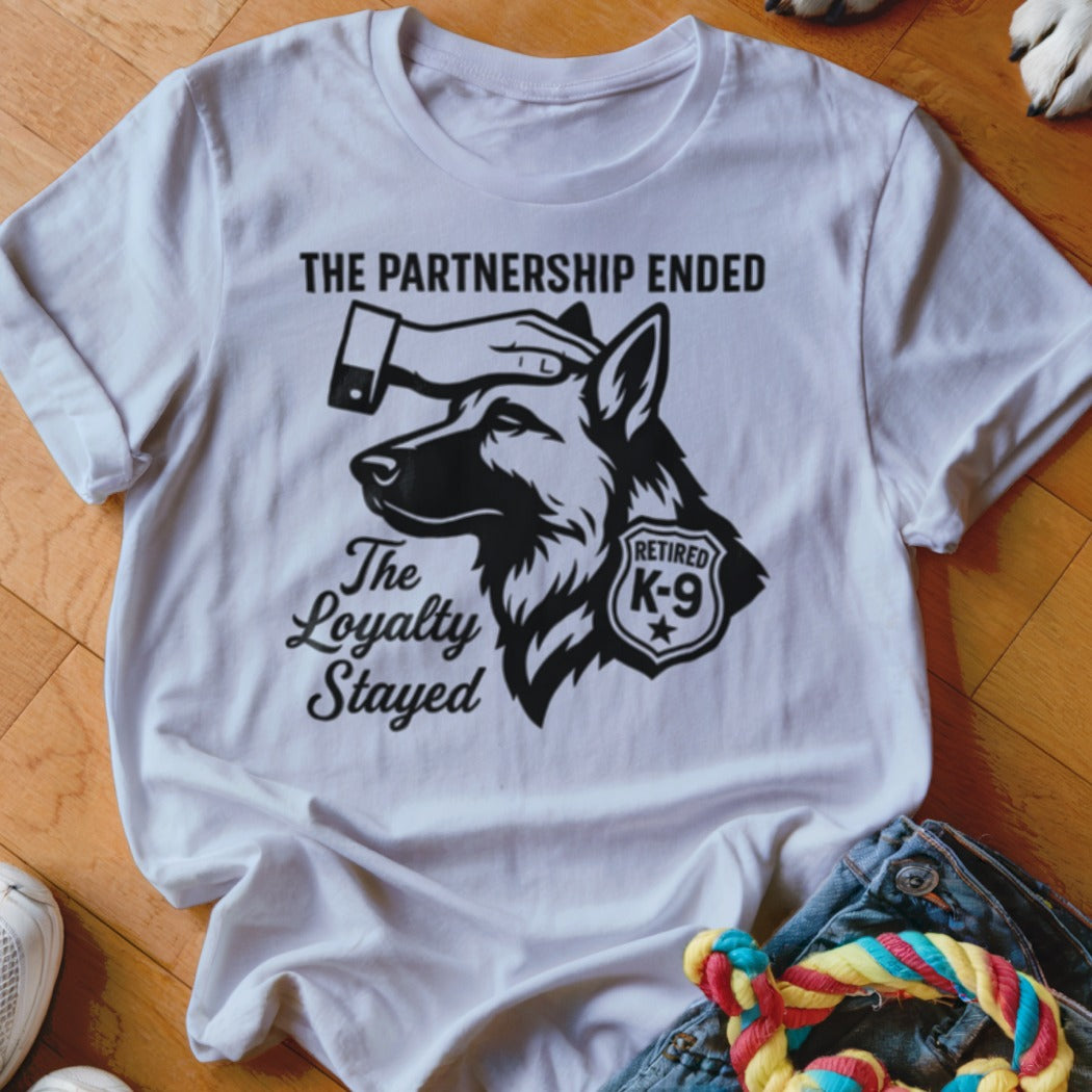 White t-shirt with graphic of a German Shepherd, hand petting head, text: "The Partnership Ended. The Loyalty Stayed. Retired K-9."