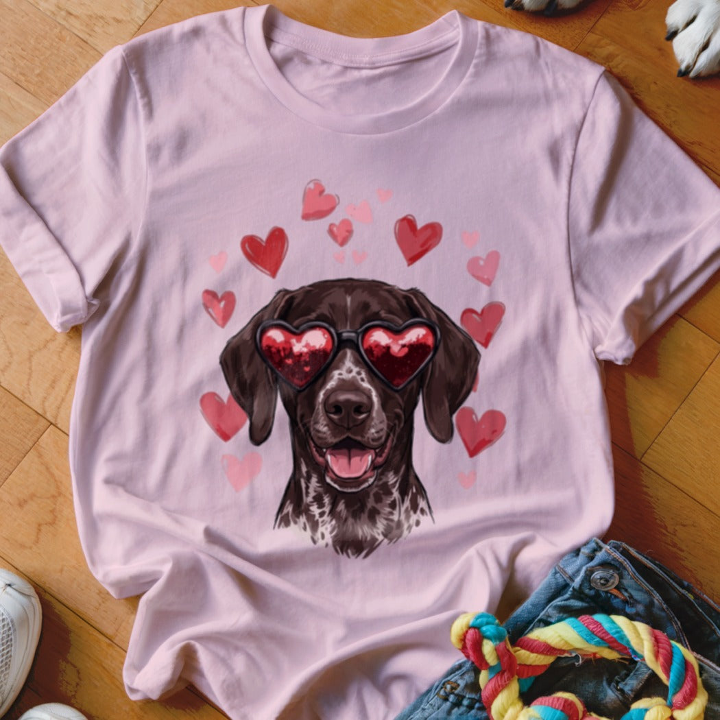 A light pink t-shirt features a graphic of a brown dog wearing heart-shaped sunglasses, surrounded by floating red hearts.