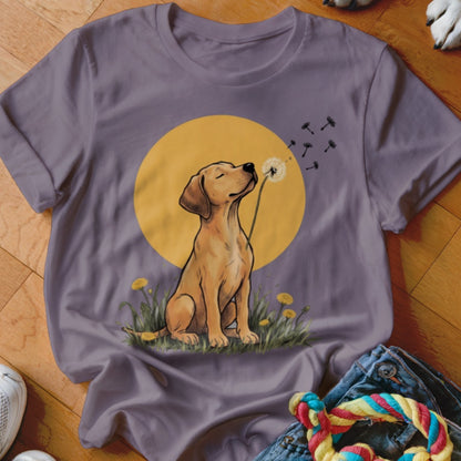 A purple crewneck t-shirt featuring an illustration of a yellow Labrador puppy blowing dandelion seeds.