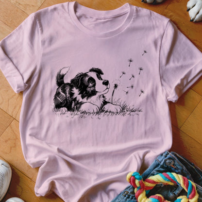 Light pink crewneck t-shirt featuring a black graphic of a puppy watching dandelion seeds blow away.