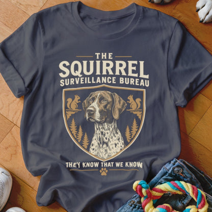 A dark gray crewneck t-shirt featuring a dog graphic, text reading THE SQUIRREL SURVEILLANCE BUREAU, and pine trees.