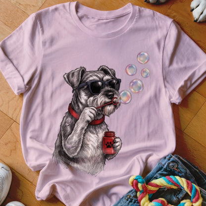 A pink t-shirt featuring a graphic of a Schnauzer wearing sunglasses and blowing soap bubbles.
