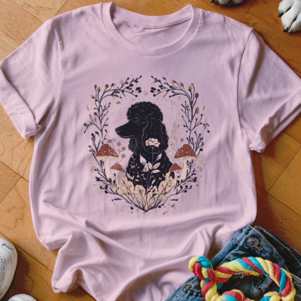 A light pink t-shirt with a graphic of a black poodle surrounded by mushrooms and foliage.
