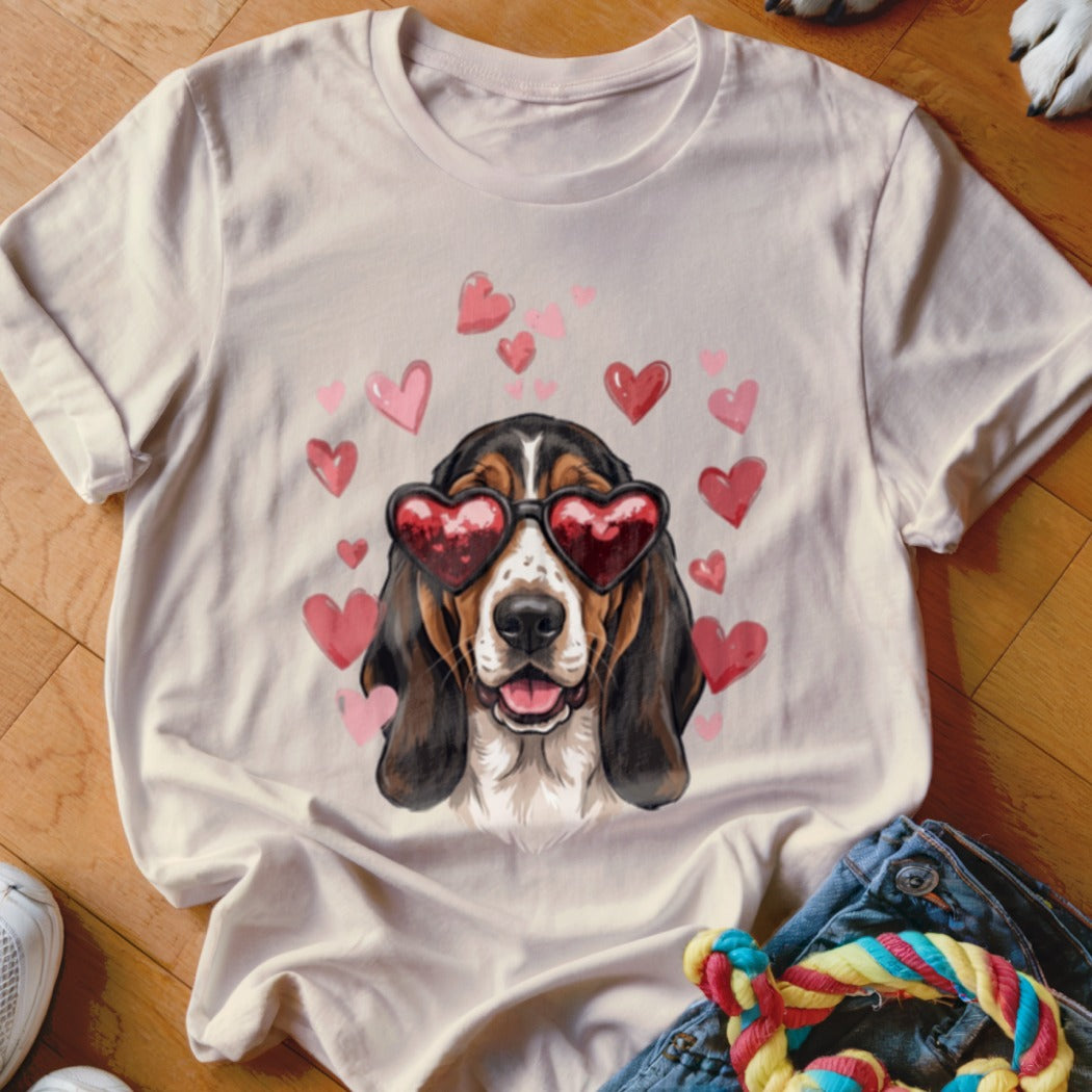 A light pink t-shirt features a basset hound wearing heart-shaped sunglasses surrounded by pink hearts.