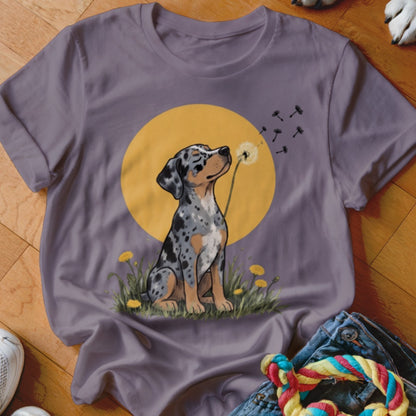 Muted purple t-shirt featuring a graphic of a merle puppy blowing dandelion seeds against a yellow circle background.