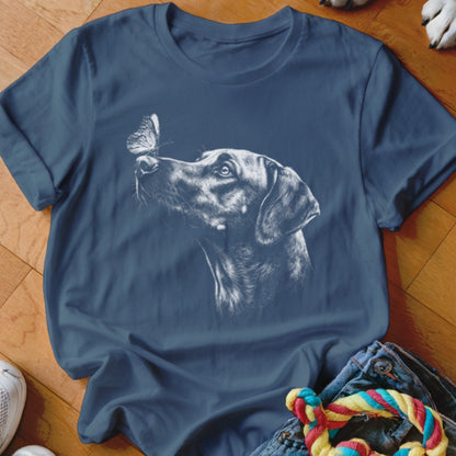 A blue t-shirt printed with a white graphic of a dog looking at a butterfly on its nose.