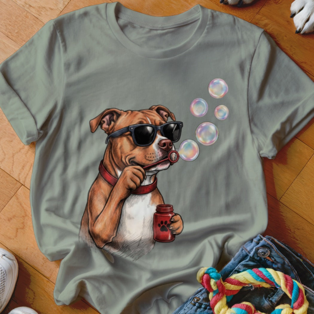 Sage green t-shirt featuring a graphic of a brown dog wearing sunglasses and blowing soap bubbles.