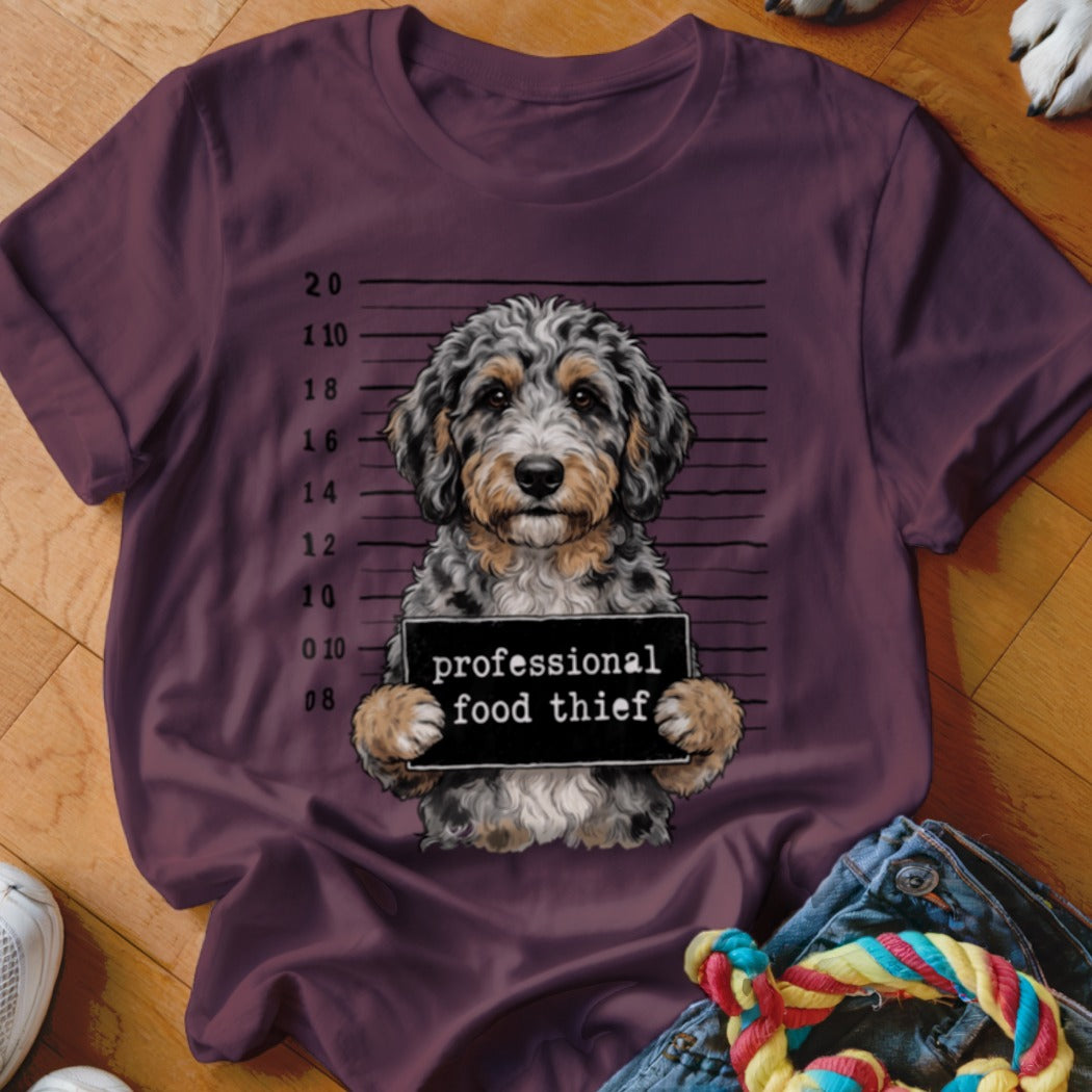 Bernedoodle with "professional food thief" sign on a mugshot background.