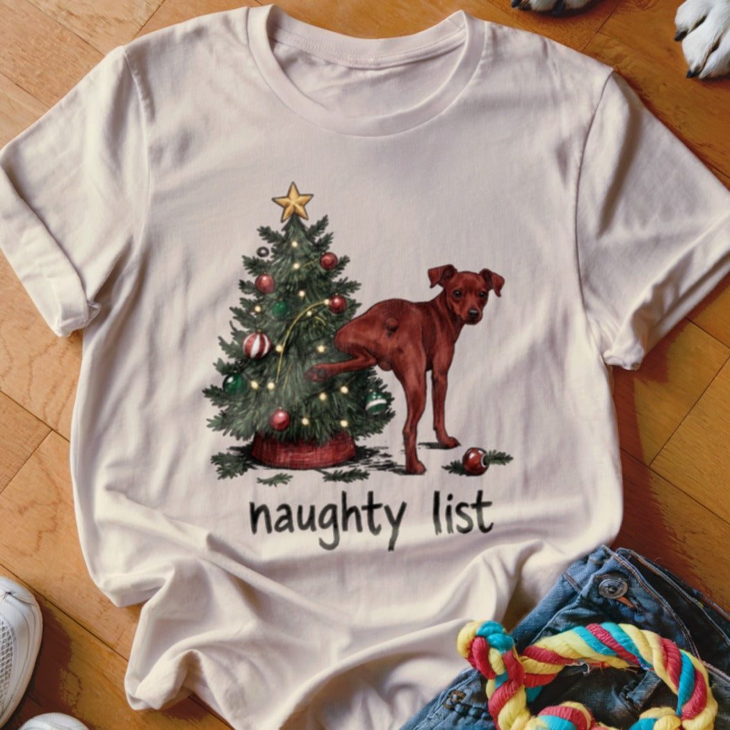 White t-shirt with a graphic of a dog near a Christmas tree, text reads "naughty list".