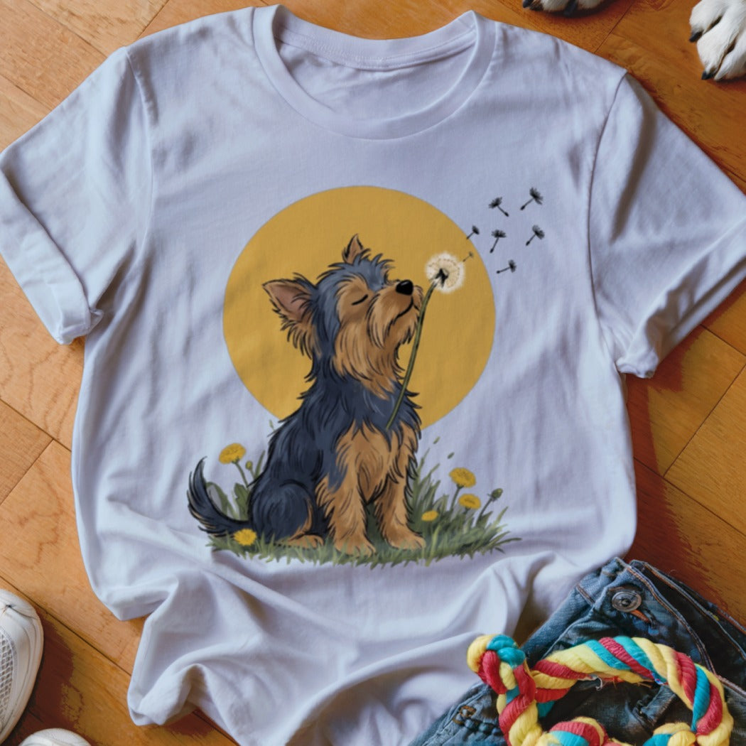 A white t-shirt featuring an illustration of a Yorkshire terrier blowing dandelion seeds.