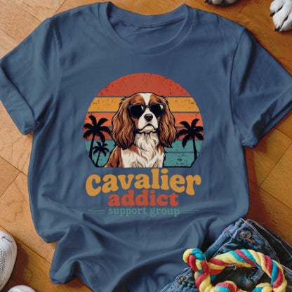 Blue t-shirt featuring a retro graphic of a Cavalier King Charles Spaniel in sunglasses before sunset stripes.
