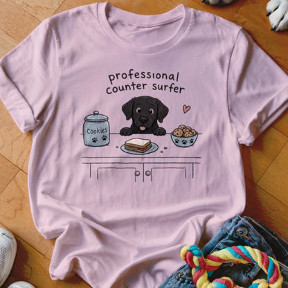 Pink t-shirt with cartoon of black lab on counter with cookies and sandwich.