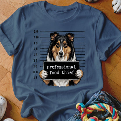 Tricolor dog mugshot with "professional food thief" sign on blue t-shirt.