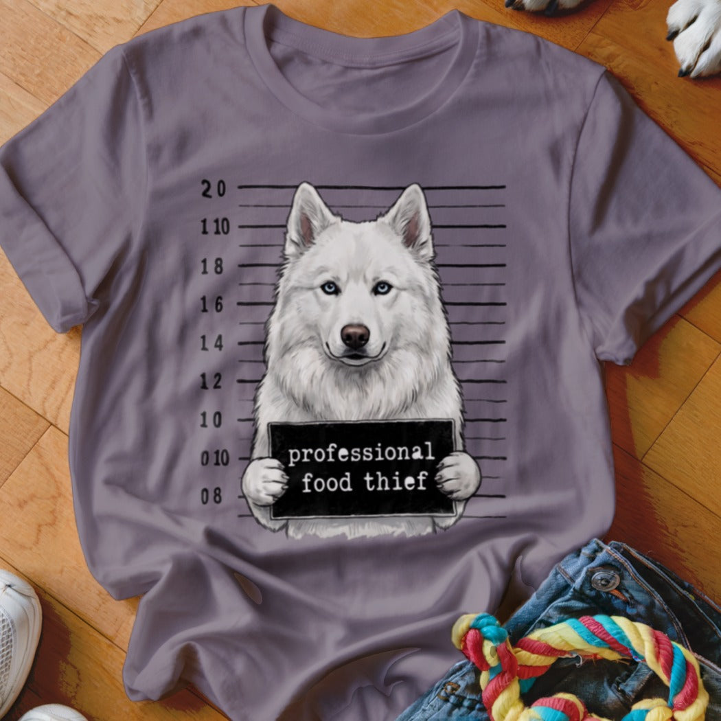 White husky mugshot with "professional food thief" sign on a t-shirt.