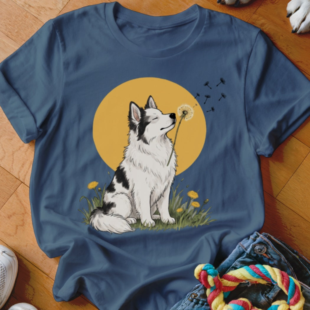 A blue t-shirt featuring an illustration of a black and white dog blowing dandelion seeds.