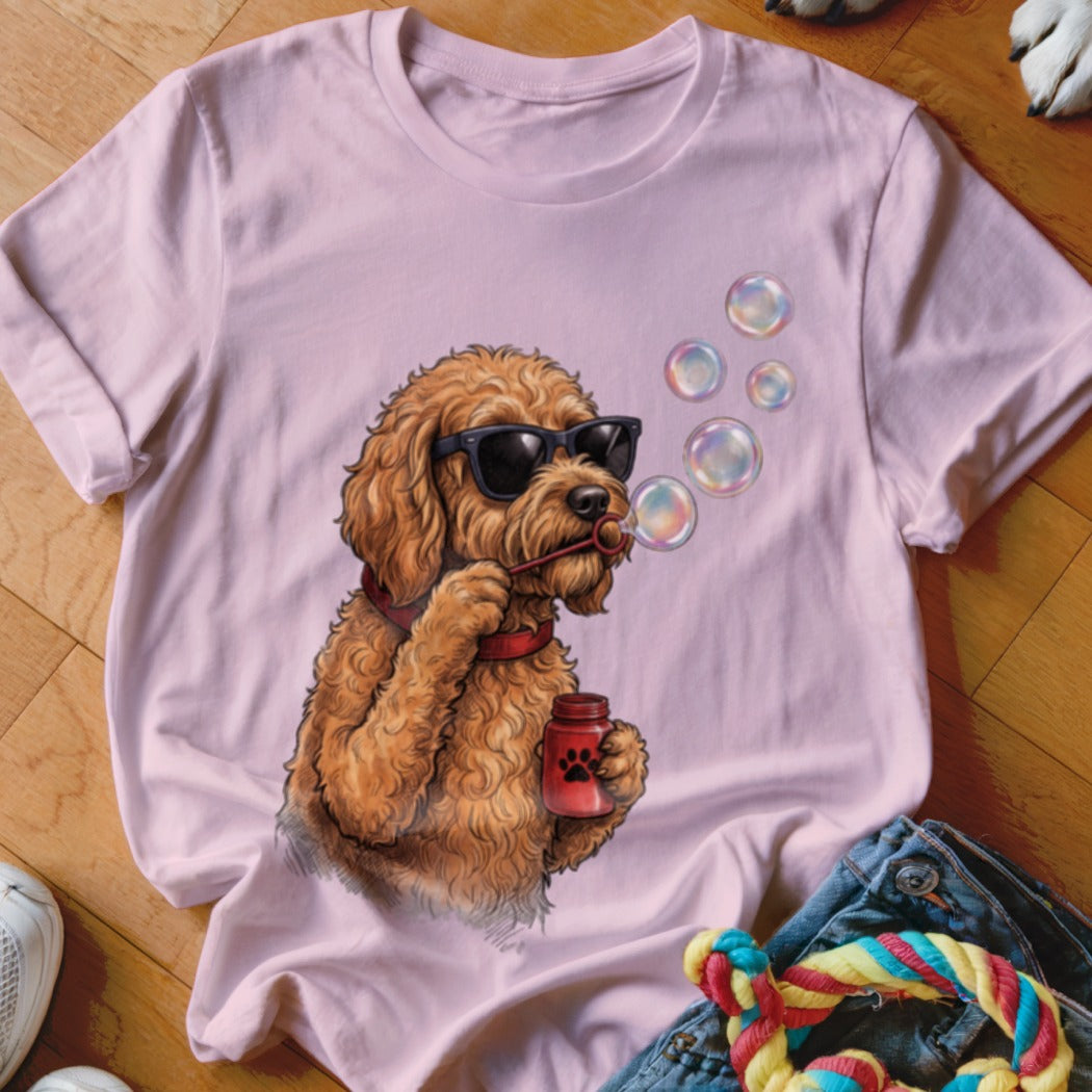 Light pink t-shirt featuring a graphic of a fluffy brown dog wearing sunglasses and blowing soap bubbles.