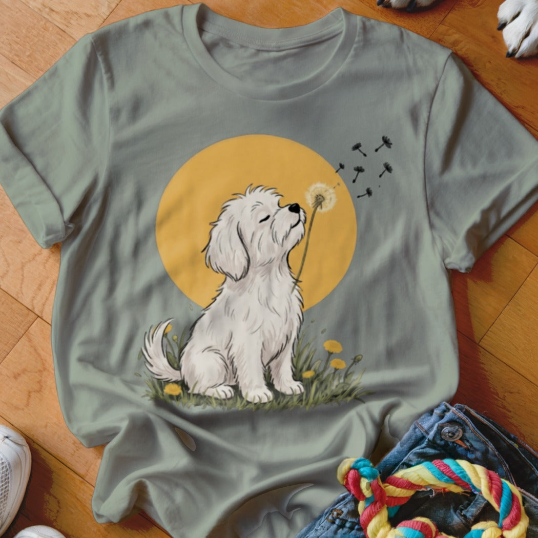 Sage green t-shirt featuring a cartoon graphic of a white puppy blowing dandelion seeds.