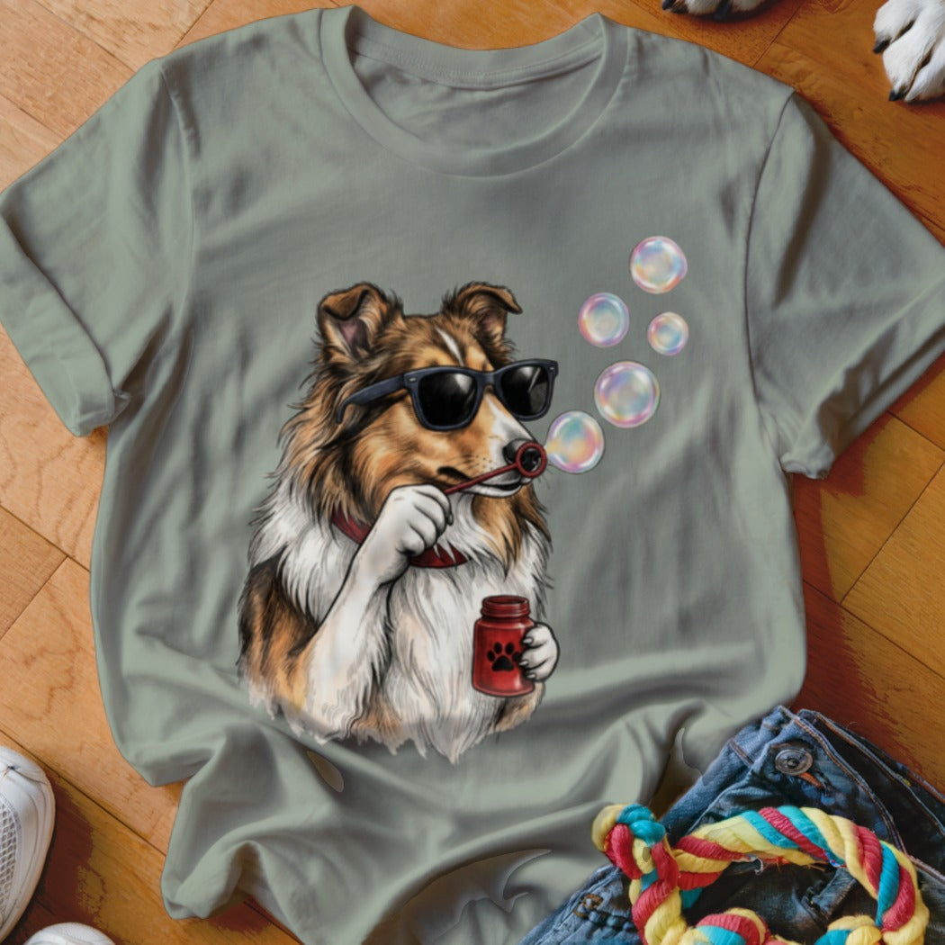 An olive green t-shirt featuring a graphic of a Sheltie dog wearing sunglasses and blowing bubbles.