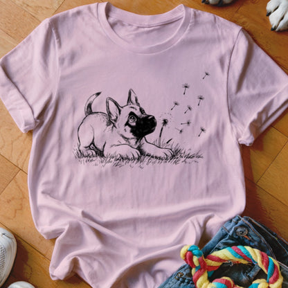 A pink crewneck t-shirt featuring a black line drawing of a puppy looking at floating dandelion seeds.